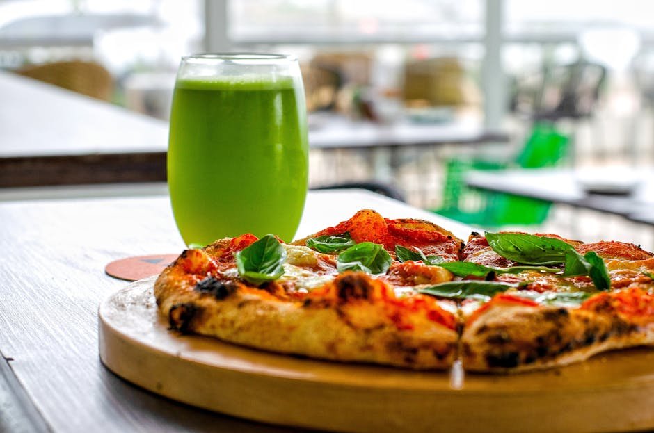 Glass of green juice and pizza side by side on a table, symbolizing balance and questioning if a wellness routine in midlife is truly working